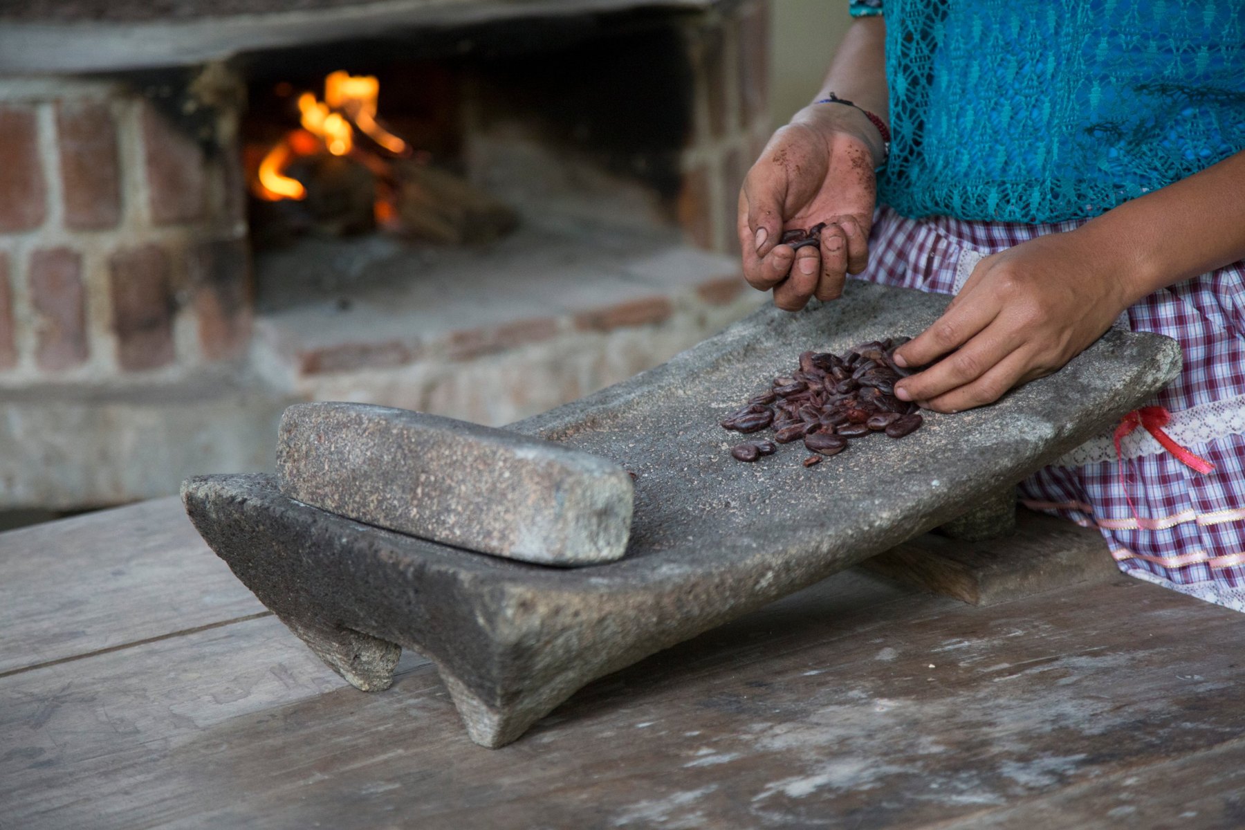 Geröstete Kakaobohnen auf dem Metate, dem Mahlstein, vor dem offenen Feuer